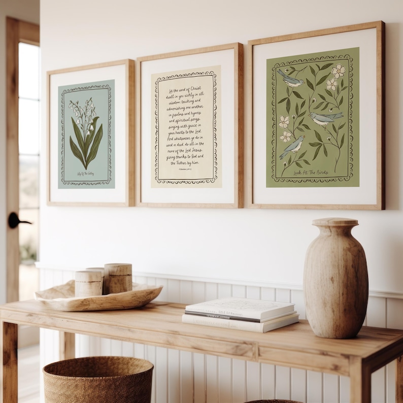 May include: Three framed art prints with botanical and text designs. The prints are in light wood frames and feature illustrations of flowers, birds, and text. The color palette includes shades of green, blue, and cream, creating a calming aesthetic.