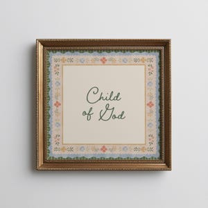 May include: A framed print featuring the text "Child of God" in a cursive font. The print has a cream background with a floral border in blue, pink, and yellow. The frame is a gold colour.
