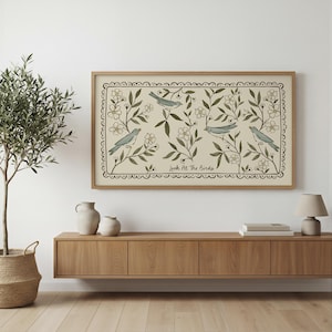 May include: A framed artwork featuring a beige background with a floral and bird design. The artwork has a light brown wooden frame. The design includes blue birds, white flowers, and green leaves. The text "Look At The Birds" is at the bottom.