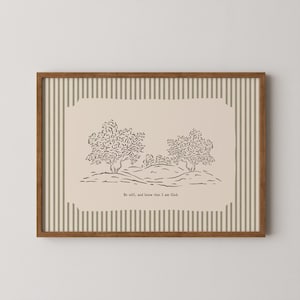 Puede incluir: Una impresión artística enmarcada con una ilustración minimalista de paisaje de árboles y una colina en tinta negra. La obra de arte está sobre un fondo beige con un borde a rayas. El texto "Be still, and know that I am God" está en la parte inferior.