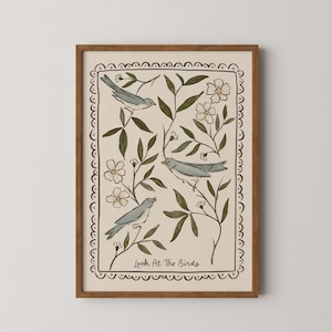 Könnte beinhalten: Gerahmter Kunstdruck mit drei hellblauen Vögeln zwischen grünen Blättern und weißen Blüten. Das Kunstwerk hat einen cremefarbenen Hintergrund und eine dekorative Bordüre. Der Text "Look At The Birds" befindet sich unten. Der Rahmen ist braun.