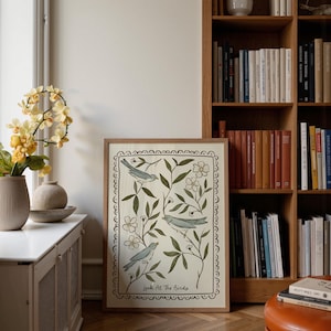 Pu&ograve; includere: Una stampa artistica incorniciata con tre uccelli blu tra foglie verdi e fiori bianchi. L'opera d'arte &egrave; bordata da un bordo decorativo e include il testo "Look At The Birds" in basso. La stampa &egrave; esposta vicino a una finestra e a una libreria.