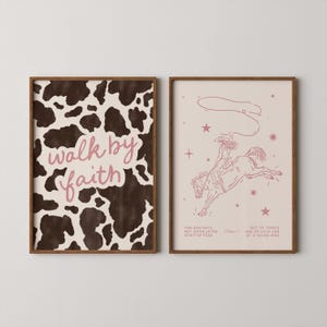 May include: Two framed art prints. One has a cowhide pattern with the words "walk by faith" in pink. The other print shows a rodeo scene with a cowboy on a bucking horse, with text below.