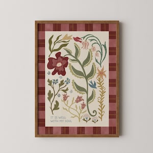 May include: A framed art print with a floral design in red, green, and yellow on a cream background. The print is bordered by a red plaid pattern. The text "IT IS WELL WITH MY SOUL" is included in the design. The frame is made of wood.