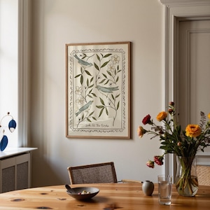 Pu&ograve; includere: Una stampa artistica incorniciata con tre uccelli blu tra foglie verdi e fiori bianchi. L'opera d'arte ha uno sfondo color crema e un bordo decorativo smerlato. Il testo "Look At The Birds" &egrave; in basso.