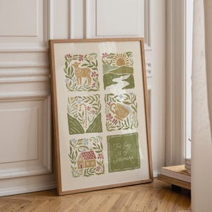 May include: A framed print with a light wood frame. The artwork features six illustrated squares with a lamb, landscape, chalice, house, and text that reads "The Lord is my Shepherd". The illustrations are in shades of green, beige, and brown.