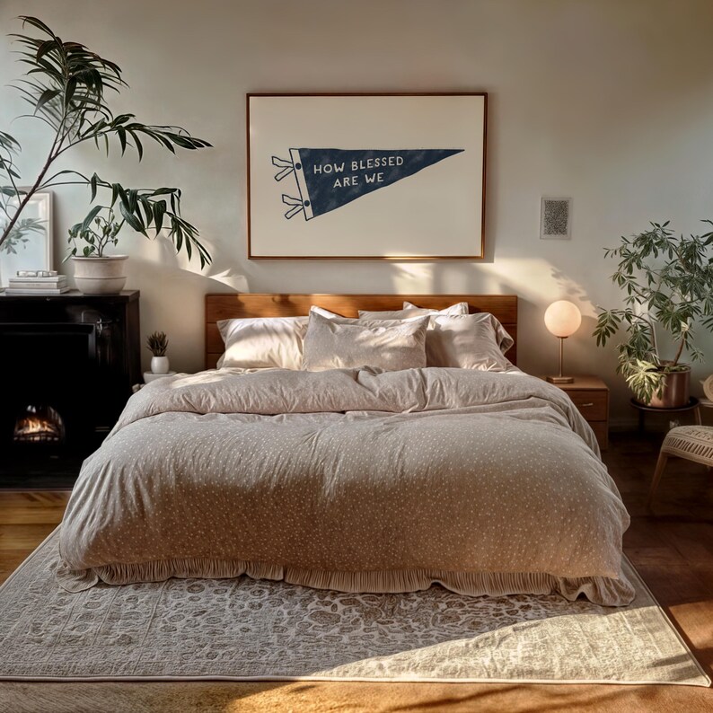 K&ouml;nnte beinhalten: Ein Schlafzimmer mit einem Bett, das mit einer beigen Bettdecke und Kissen mit wei&szlig;em Punktmuster ausgestattet ist. Ein gerahmtes Banner mit der Aufschrift "HOW BLESSED ARE WE" h&auml;ngt &uuml;ber dem Bett. Der Raum ist mit Pflanzen und einem Teppich dekoriert.