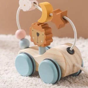 May include: A wooden toy pull-along car with a lion face, a moon, a star, and beads. The car has blue wheels and a white cord.