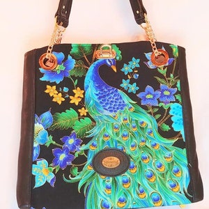 May include: A black tote bag with a peacock and floral design. The bag has a gold chain strap and a black leather trim.