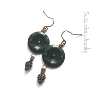 May include: A pair of green button earrings with a small gold pine cone charm hanging from each button.