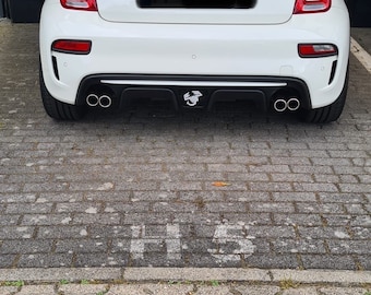 Può includere: Una Fiat 500 Abarth bianca con un paraurti posteriore nero e due scarichi. L'auto ha uno spoiler posteriore nero e un diffusore posteriore nero. L'auto è parcheggiata su un vialetto di mattoni grigi.