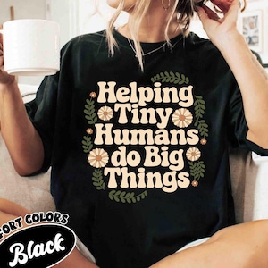 May include: Black t-shirt with a floral design and the text "Helping Tiny Humans do Big Things".