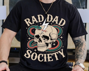 May include: Black t-shirt with the words "RAD DAD SOCIETY" in a vintage font. The graphic features a skull with a snake and lightning bolt design. The shirt is a classic crew neck style.