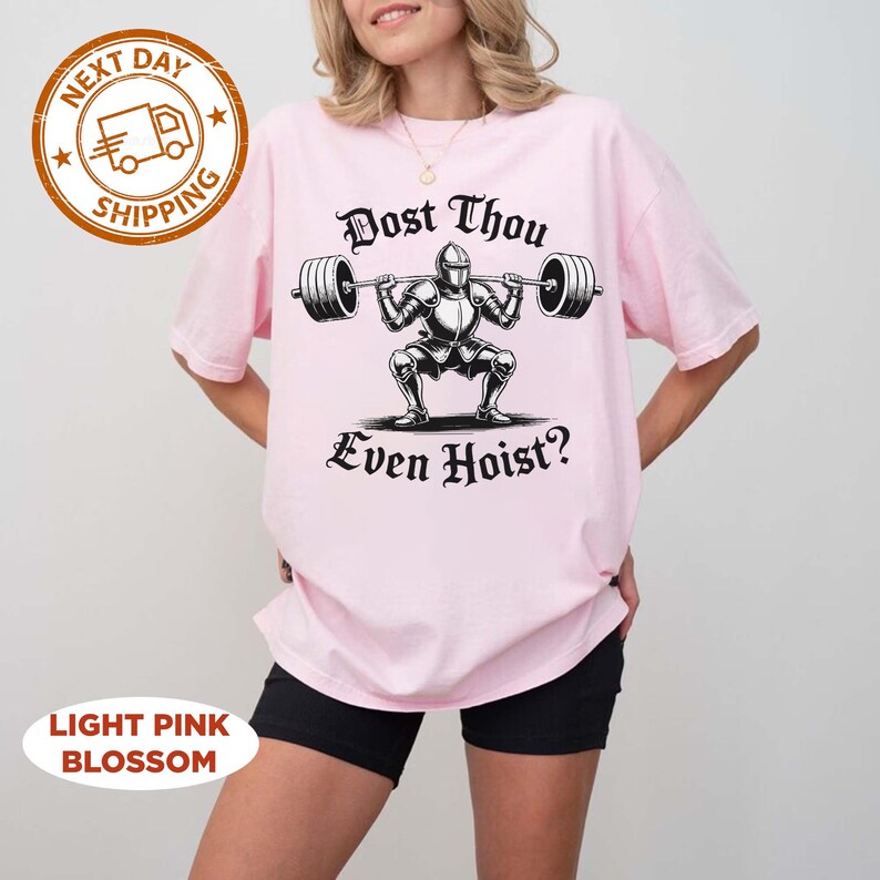 May include: Light pink t-shirt with a graphic of a knight lifting weights, and the text "Dost Thou Even Hoist?". The shirt also has a "Next Day Shipping" logo and a "Light Pink Blossom" label.