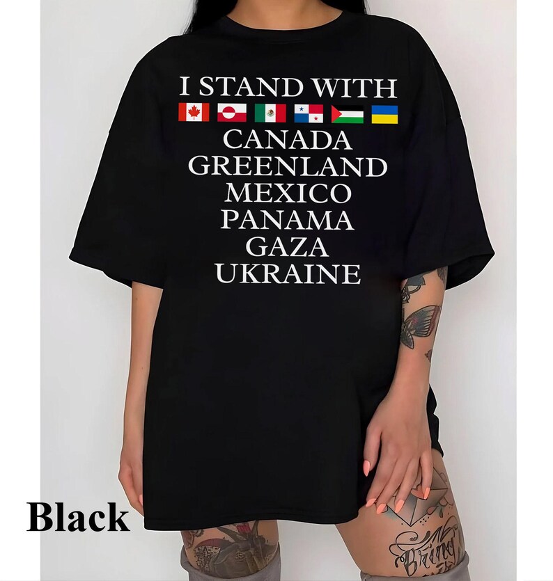 Puede incluir: Camiseta negra de gran tama&ntilde;o con el texto "I Stand With" y una fila de banderas que representan a Canad&aacute;, Groenlandia, M&eacute;xico, Panam&aacute;, Gaza y Ucrania.