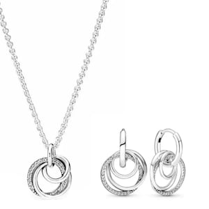 May include: A silver necklace and matching earrings set. The necklace has a pendant with three interlocking circles, one encrusted with small clear stones. The earrings have a similar design, with three interlocking hoops.