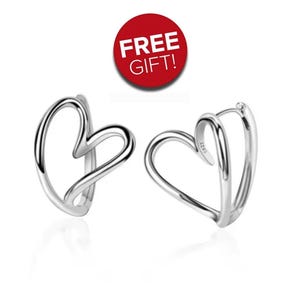 Puede incluir: Un par de pendientes de aro plateados con forma de corazón. Los pendientes son de metal brillante y tienen un diseño minimalista. Un círculo rojo con el texto "FREE GIFT!" está en el fondo.
