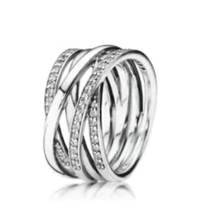 May include: A silver ring with an intricate, interwoven design. The ring comprises multiple bands that overlap, some set with small, clear gemstones. The ring has a polished, reflective surface, creating a modern aesthetic.