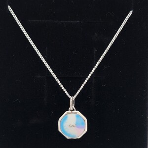 May include: A silver necklace with a small, octagonal pendant. The pendant has a white, blue, and pink iridescent design with a small infinity symbol in the center. The chain is a delicate, linked style.