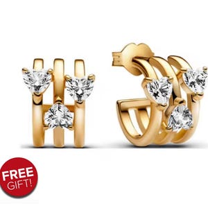 May include: Gold-coloured hoop earrings featuring heart-shaped clear gemstones. The earrings have a layered design with multiple hoops and heart-shaped stones. The image also includes a red circle with the text "FREE GIFT!"