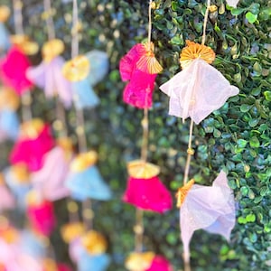 May include: A garland of pink, blue, and white fabric flowers with gold accents hanging against a green backdrop.