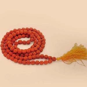 Puede incluir: Una larga hebra de cuentas rojas con un borla de hilo amarillo y naranja. Las cuentas están hechas de materiales naturales y se utilizan para la oración o la meditación.
