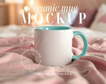 May include: A white ceramic mug with a light blue rim and handle, sitting on a pink fabric surface. The text "ceramic mug MOCKUP" is written in white on a blurred background.