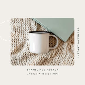 May include: White enamel mug with a black rim sitting on a beige knitted blanket. The mug is empty and has a handle. A green book is partially visible in the background.