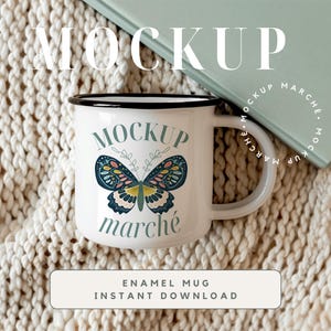 May include: White enamel mug with a black rim and handle. The mug has a butterfly graphic with the text "MOCKUP march&eacute;" printed on it. The mug is sitting on a white knitted blanket.