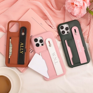 May include: Three personalized phone cases in brown, pink, and green. Each case has a card slot and a strap with a name on it. The brown case has a black strap with "ALLY". The pink case has a white strap with "W.N.L". The green case has a pink strap with "Bonnie".