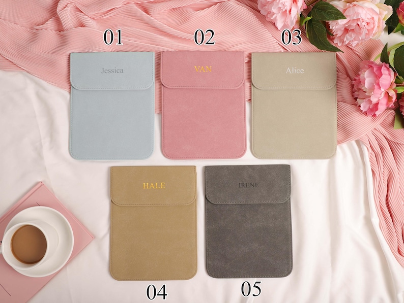 May include: Five personalised laptop sleeves in pastel shades: light blue, pink, beige, tan, and grey. Each sleeve features a flap closure and an embroidered name: Jessica, Van, Alice, Hale, and Irene. The sleeves are arranged on a pink fabric.