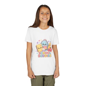 Könnte beinhalten: Ein weißes T-Shirt mit einer bunten Grafik von Cartoon-Schulmaterialien, darunter ein Notizbuch, ein Rucksack, ein Bleistift und ein Apfel mit dem Text SCHOOL BUDDIES. Das Design verwendet Pastellfarben sowie kleine Herz- und Sternakzente.