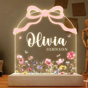 May include: A pink and white personalized night light with a bow on top. The light features a floral design and the name "Olivia Johnson" in white text.