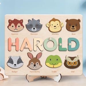 May include: Wooden puzzle featuring animal faces and the name "HAROLD" in colorful letters. Includes a squirrel, raccoon, monkey, bear, badger, hare bunny, snake, and owl. The puzzle is designed for educational play.