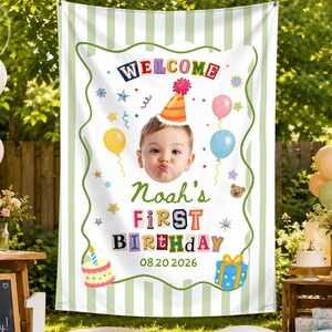 May include: A white fabric banner with light green vertical stripes featuring a colorful graphic of a child wearing a party hat, surrounded by balloons, stars, and a cake. The text reads Welcome, Noah's First Birthday, and 08.20.2026.