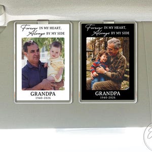 May include: Two rectangular car visor ornaments. One has a white background with a photo of a man holding a baby, and the text "Forever in my heart, Always by my side, Grandpa 1940-2026." The other has a black background with a photo of a man holding a child, and the same text.