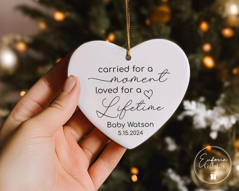 May include: White heart-shaped ornament with the text "carried for a moment loved for a lifetime" and the name "Baby Watson" and the date "5.15.2024".