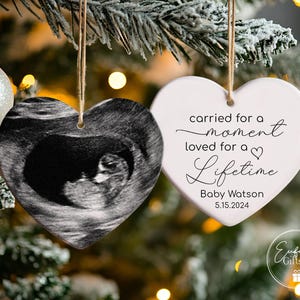 May include: Two white heart-shaped Christmas ornaments. One ornament features a black and white ultrasound image of a baby. The other ornament has the text "carried for a moment loved for a lifetime" with the name "Baby Watson" and the date "5.15.2024".