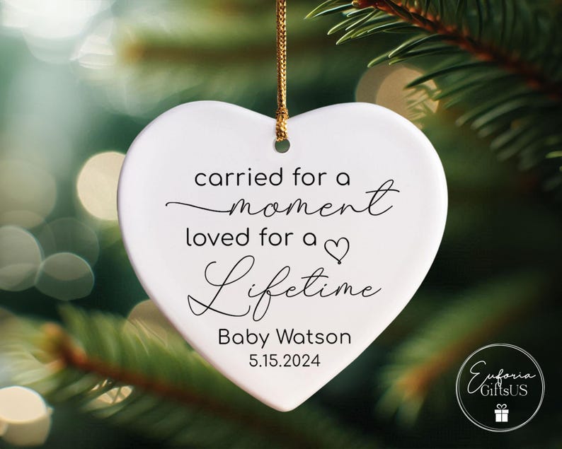 May include: White heart-shaped ornament with the text "carried for a moment loved for a lifetime" and the name "Baby Watson" and the date "5.15.2024".