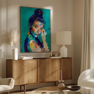 May include: A colorful portrait of a woman with dark hair in a bun, set against a teal background. The artwork features vibrant brushstrokes of red, yellow, and blue. The painting is displayed above a wooden cabinet with a lamp and decorative items.