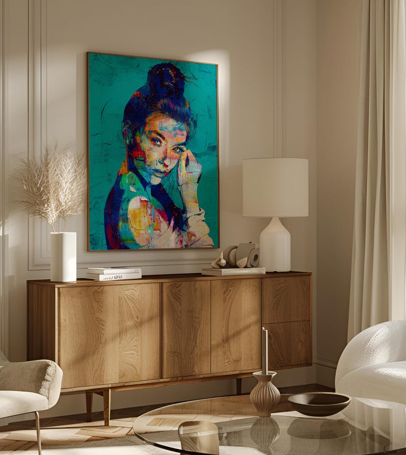 May include: A colorful portrait of a woman with dark hair in a bun, set against a teal background. The artwork features vibrant brushstrokes of red, yellow, and blue. The painting is displayed above a wooden cabinet with a lamp and decorative items.
