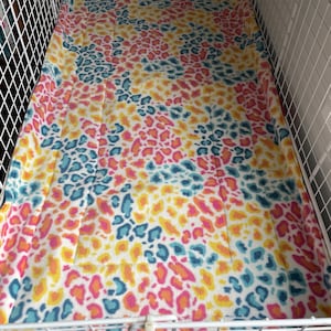 May include: A colourful animal print fleece liner for a small animal cage. The liner is made of soft, comfortable fabric and features a variety of colours, including pink, yellow, blue, and white.