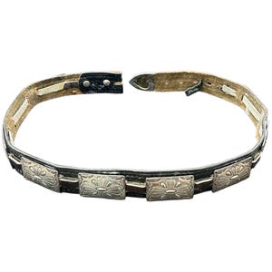May include: A vintage belt with a black leather strap and silver-toned rectangular embellishments. Each embellishment features a floral design. The belt has a buckle closure and is open, showing the interior construction.