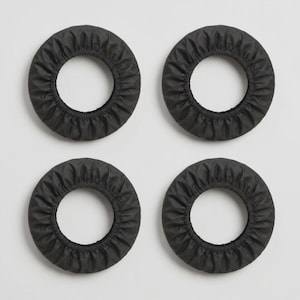 K&ouml;nnte beinhalten: Vier kreisf&ouml;rmige schwarze Stoffabdeckungen mit elastischem, gerafftem Rand. Diese ringf&ouml;rmigen Schutzh&uuml;llen haben eine glatte, matte Textur und eine einheitliche dunkelgraue Farbe, angeordnet in einem zwei-mal-zwei Rastermuster.