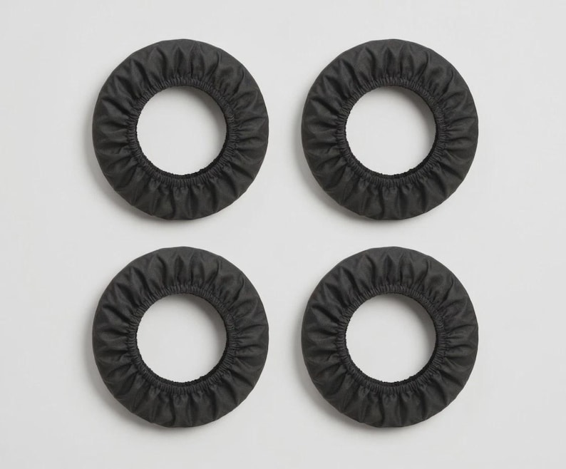 K&ouml;nnte beinhalten: Vier kreisf&ouml;rmige schwarze Stoffabdeckungen mit elastischem, gerafftem Rand. Diese ringf&ouml;rmigen Schutzh&uuml;llen haben eine glatte, matte Textur und eine einheitliche dunkelgraue Farbe, angeordnet in einem zwei-mal-zwei Rastermuster.