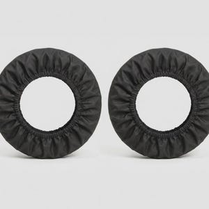 K&ouml;nnte beinhalten: Zwei kreisf&ouml;rmige Kopfh&ouml;rerbez&uuml;ge aus schwarzem Stoff mit elastischem Rand. Das Material hat eine matte Oberfl&auml;che und eine geraffte, gefaltete Textur entlang des Umfangs, die so konzipiert ist, dass sie &uuml;ber die runden Ohrpolster passt.