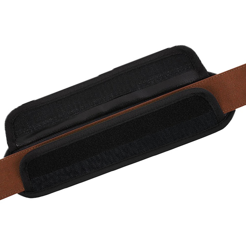 May include: A black padded strap with brown webbing. The strap has a hook and loop closure.