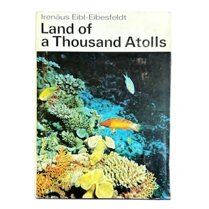 May include: A vintage book titled "Land of a Thousand Atolls" by Irenäus Eibl-Eibesfeldt. The cover features an underwater scene with colorful coral, fish, and a dark blue background. The book's title and author are in white text.