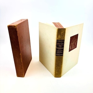 May include: Two antique books, one closed and one open. The closed book has a brown cover with worn edges. The open book displays off-white pages and a spine with gold lettering. The title "The Virginian" is visible.