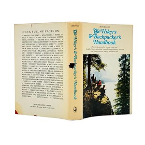 May include: Vintage book titled "The Hiker's & Backpacker's Handbook" by Bill Merrill. The cover features a scenic illustration of hikers. The book's spine lists topics like trail safety, camping, and wilderness survival. Published by Winchester Press.